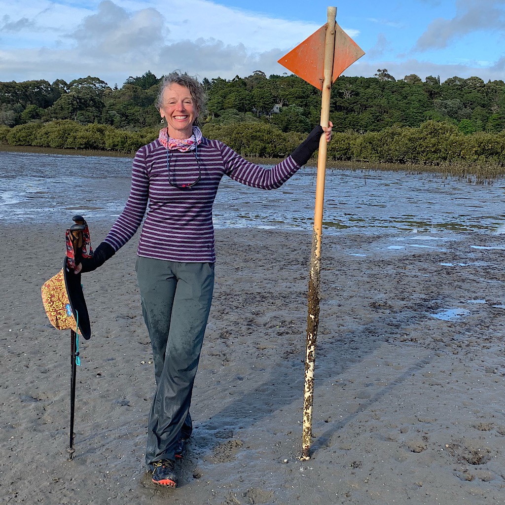 Blissful Hiker holding the TA signpost with big orange triangles pointing the way across the estuary at low tide. 