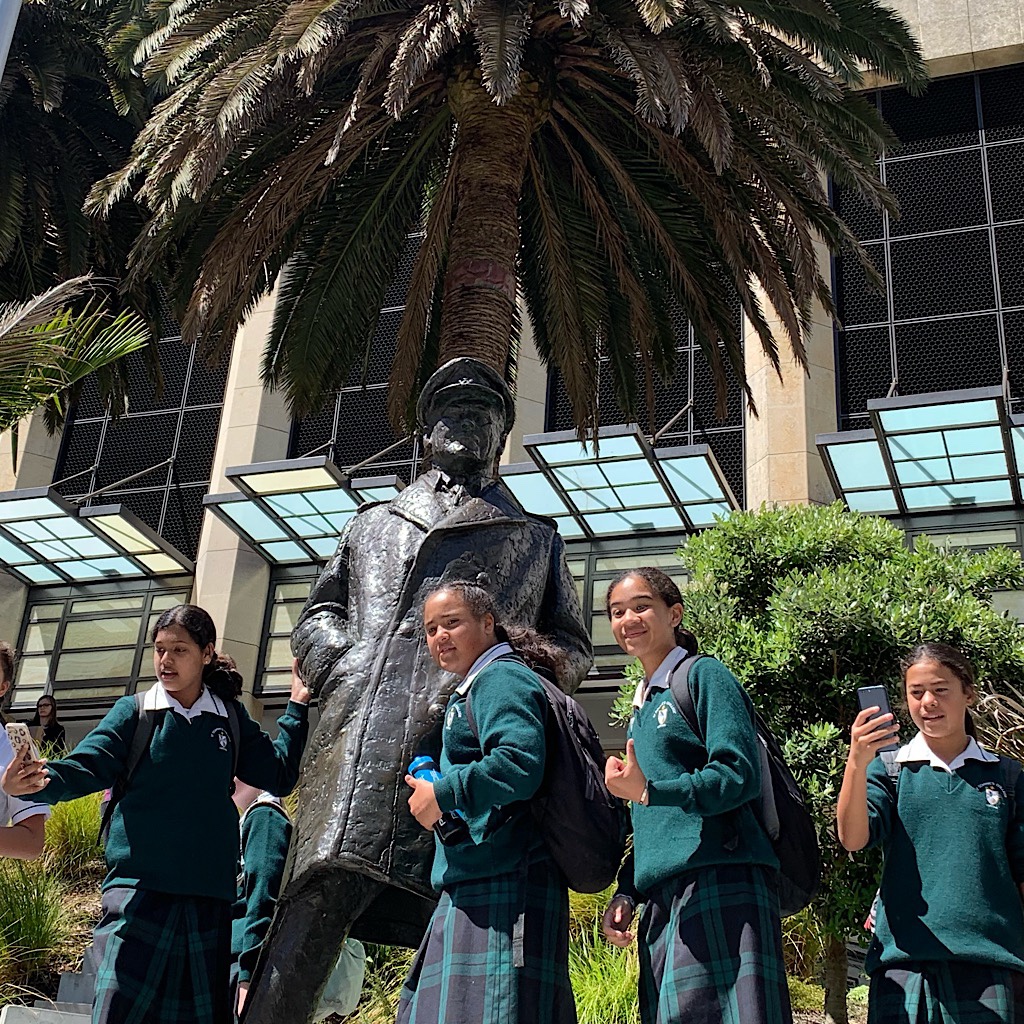 School girls take selfies next to a sea captain statue. 