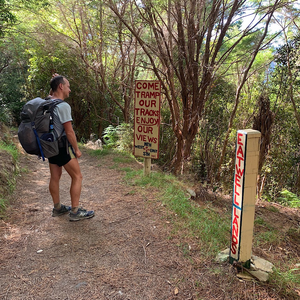 John poses in front of various signs enticing hikers to stop for  food and lodging. 