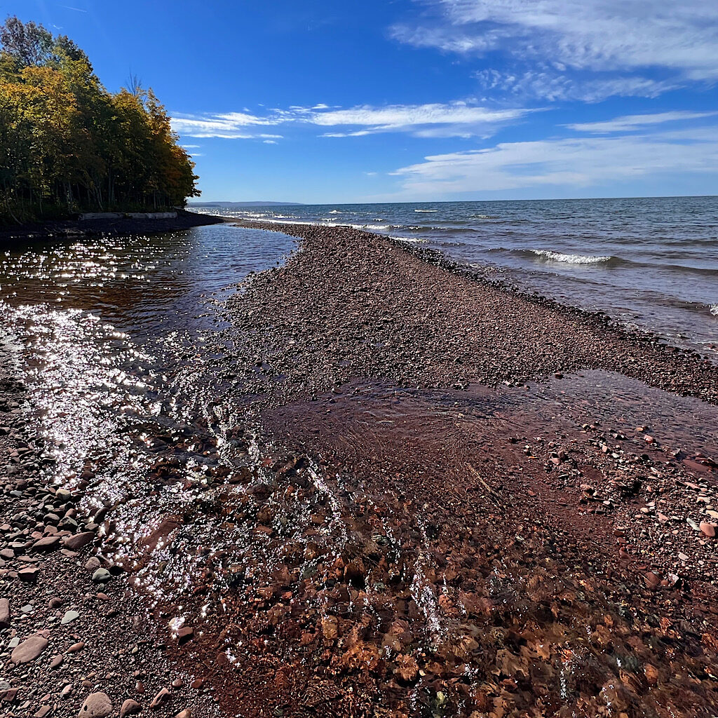 The mouth of the Big Carp River meeting a beach of tumbled and smoothed sandstone pebbles. 